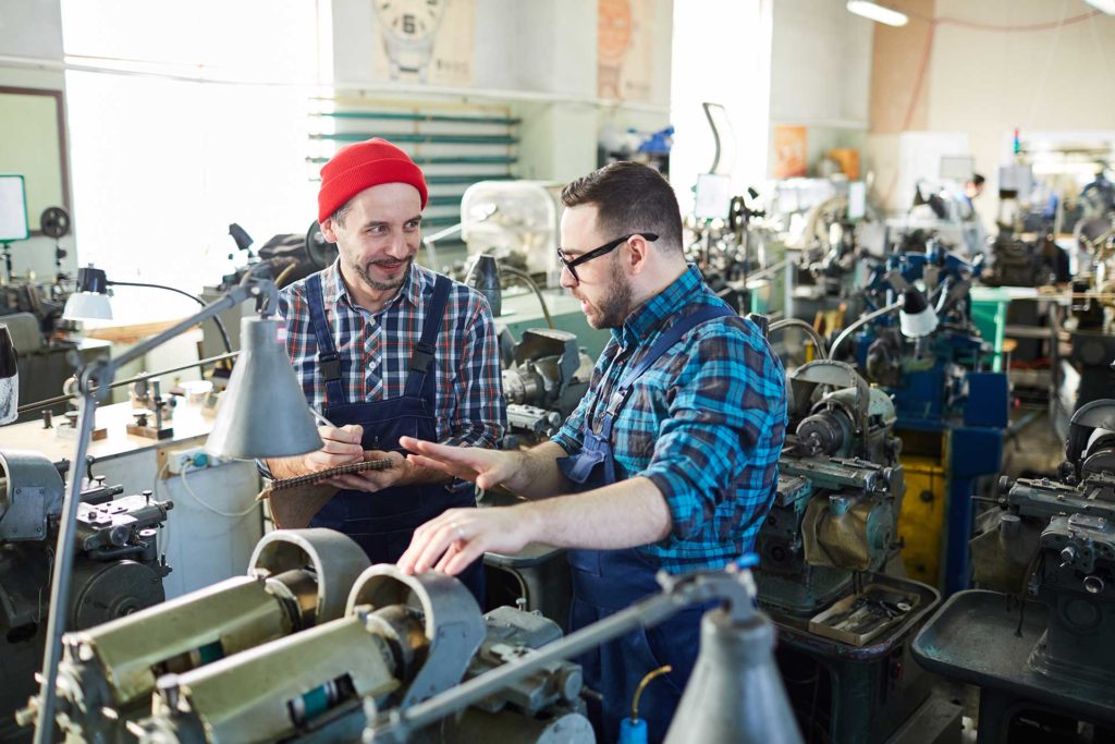 Two men are discussing a sewing machine repair in a factory